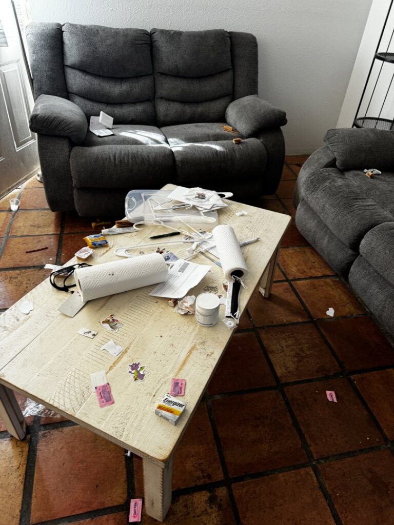 A coffee table and sofa covered in trash and clutter, indicating a junk removal service needed by Affinity Bio Solutions in Phoenix, AZ.