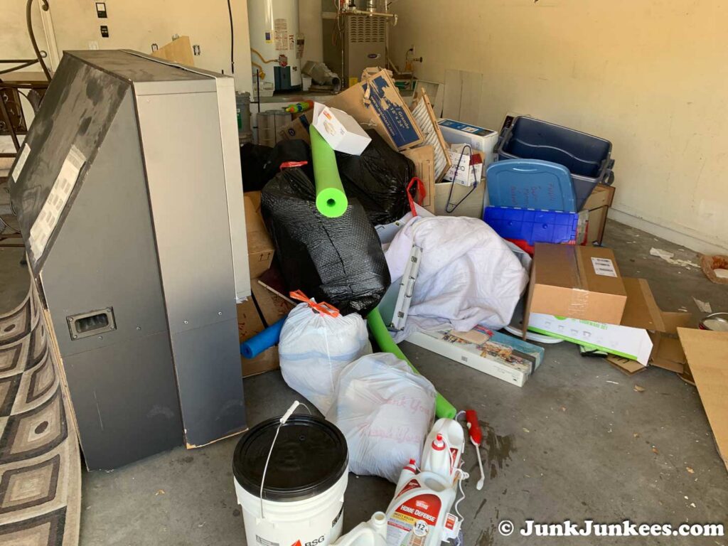 A cluttered garage filled with an old TV, trash bags, boxes, and various junk, ready for removal by Junk Junkees in Peoria, AZ.