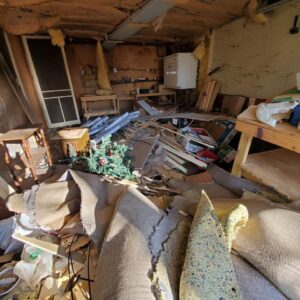 A cluttered garage filled with old furniture, wood, and boxes, representing a junk removal project for Merica JunkBoss LLC in Hammond, IN.