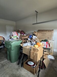 A cluttered garage filled with boxes, a trash bin, and various items, ready for junk removal by Valley Junk Removal in Huntsville, AL.