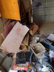 A cluttered garage floor with construction debris and junk before removal by You Call We'll Haul in Waterloo, IA.