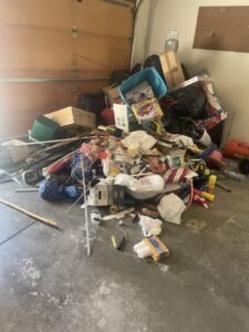 A cluttered garage floor filled with various items, boxes, and bags, awaiting junk removal by Young Bucks Junk in Shawnee, KS.