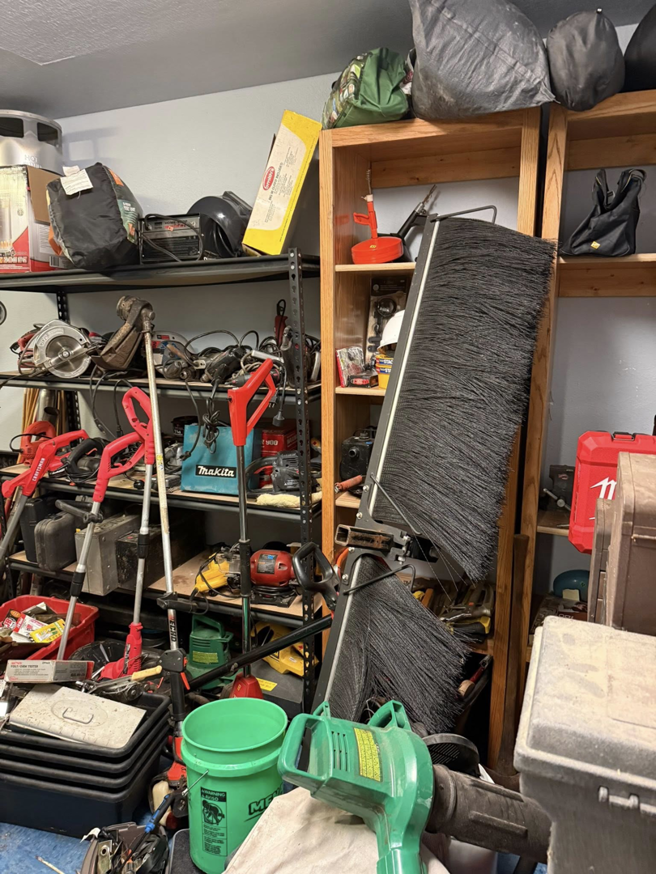 A cluttered garage filled with power tools, garden equipment, and bags, ready for cleanout by Kersten Family Junk Removal in Eau Claire, WI.