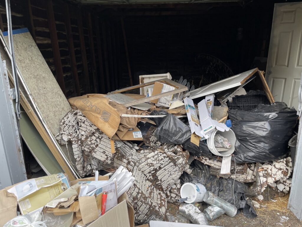 A cluttered garage interior packed with various junk, trash bags, and debris, awaiting cleanout by Prestige Junk Removal & Hauling in Detroit, MI.