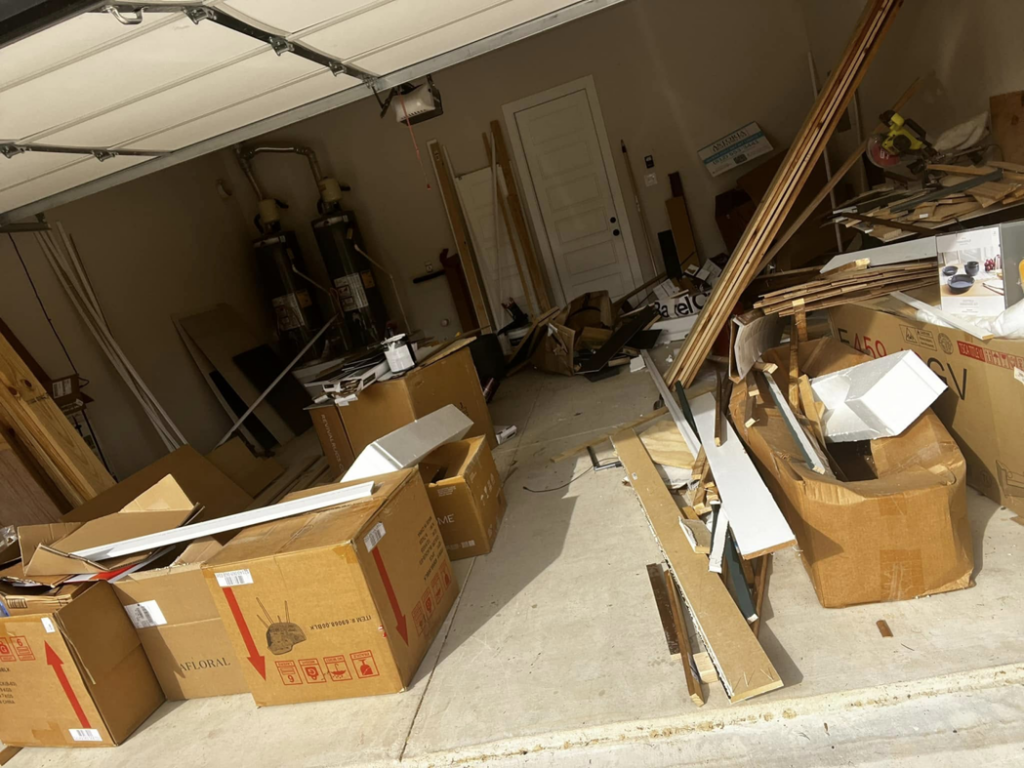 A cluttered garage filled with debris, cardboard boxes, and wood scraps, ready for junk removal by ONLY Junk Removal Services in Austin, TX.