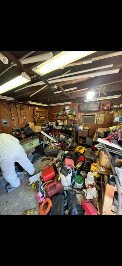 A cluttered garage before junk removal by 302-Rid-Junk in Wilmington, DE, with a worker in protective gear.