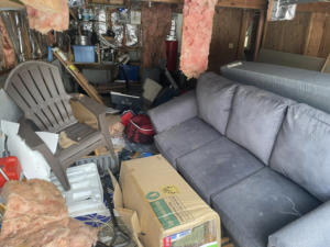 A cluttered garage filled with old furniture, insulation, and various debris, ready for a junk removal cleanout by Trash King LLC in Peoria, AZ.