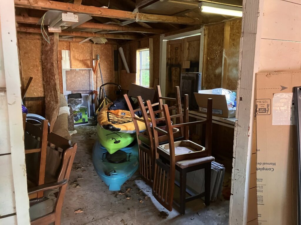 A cluttered garage or shed interior with kayaks, chairs, and boxes, indicating a space ready for junk removal by HaulPros in Erie, PA.