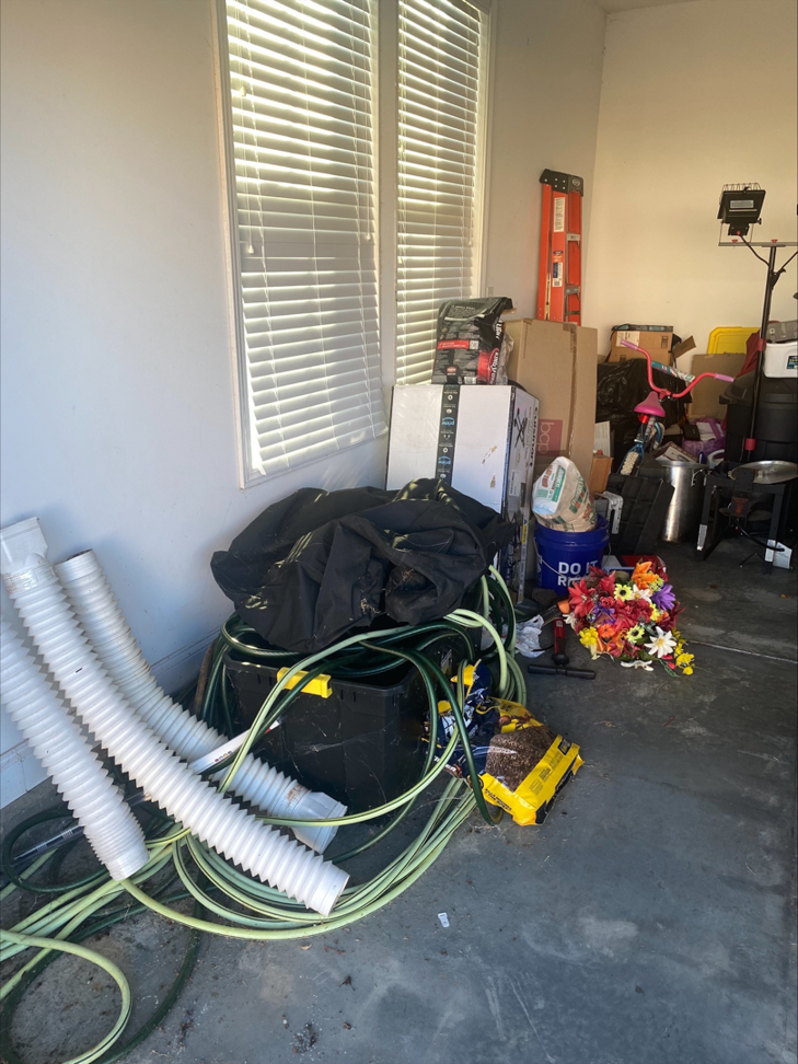 A cluttered garage filled with hoses, pipes, boxes, and various debris, ready for junk removal by Restoration Hauling Co. in Rock Hill, SC.