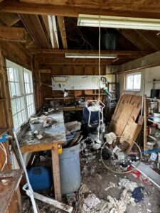 A heavily cluttered garage or workshop interior filled with debris and old items, indicating a cleanout service by Junkin Irishman in Wayne, NJ.