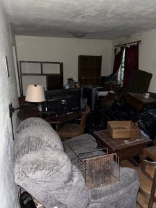 A cluttered living room with old furniture, electronics, and trash bags, awaiting a clean-out by Reliable Pro in Tallahassee, FL.