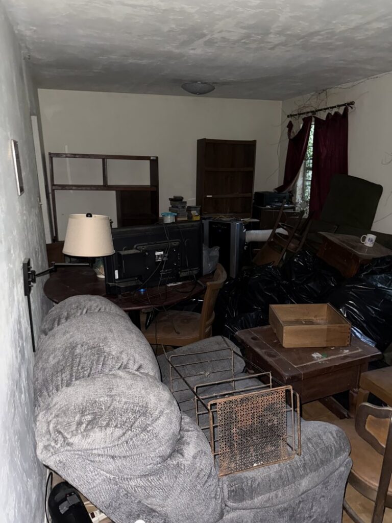 A cluttered living room with old furniture, electronics, and trash bags, awaiting a clean-out by Reliable Pro in Tallahassee, FL.