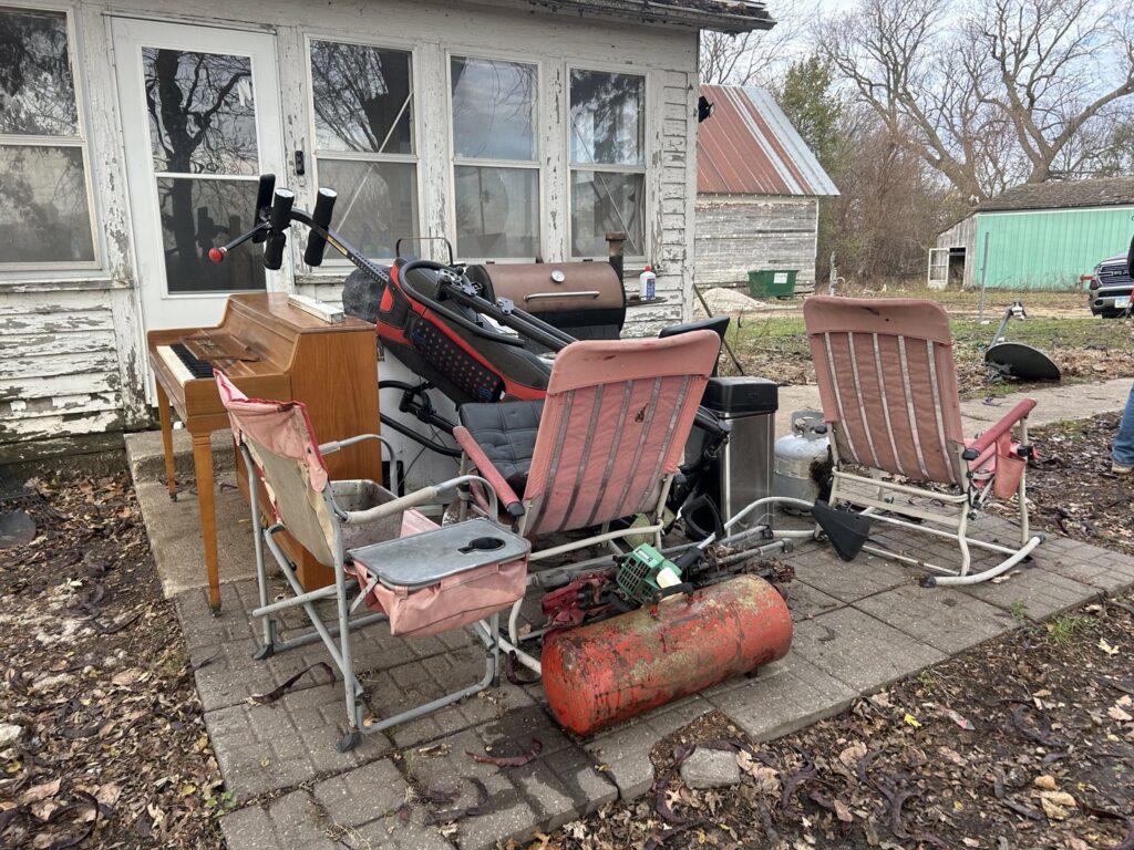 A cluttered outdoor patio with a piano, chairs, and grill before junk removal by Rosales Junk Removal in Des Moines, IA.