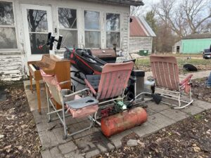 A cluttered outdoor patio with a piano, chairs, and grill before junk removal by Rosales Junk Removal in Des Moines, IA.