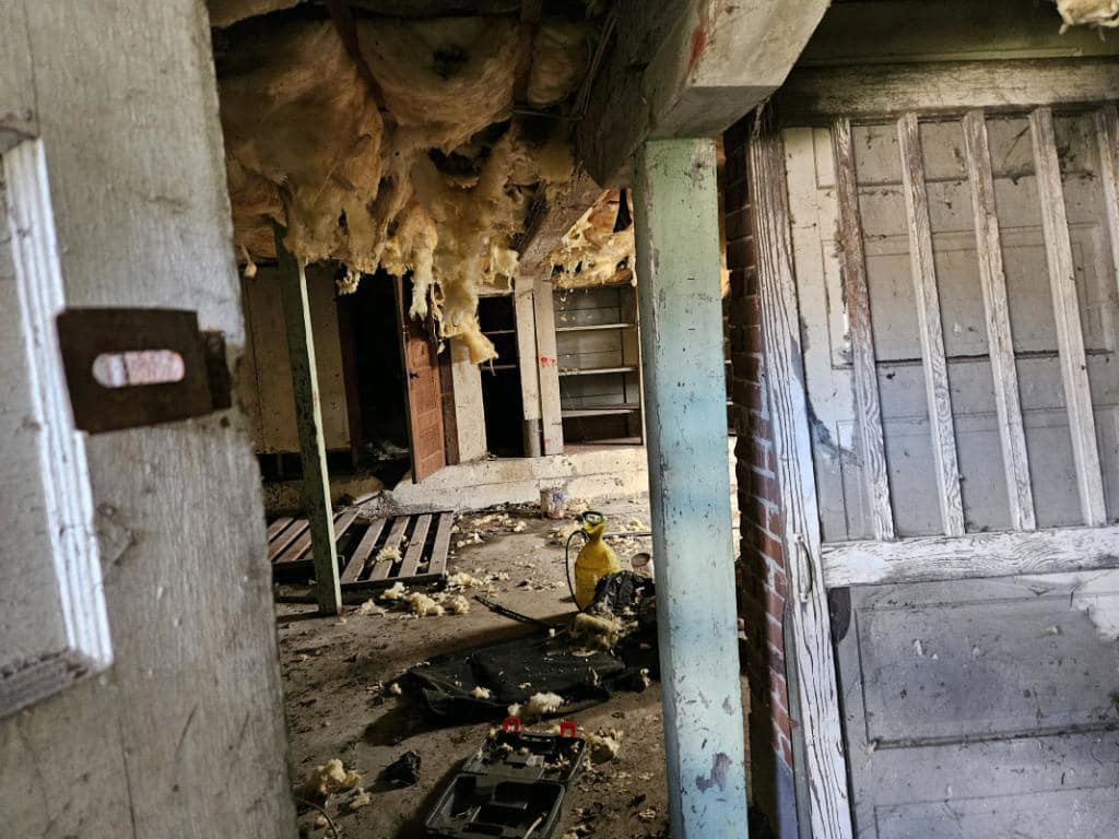 A cluttered room with debris and hanging insulation before a cleanout service by Junk Pros NW in Bellevue, WA.