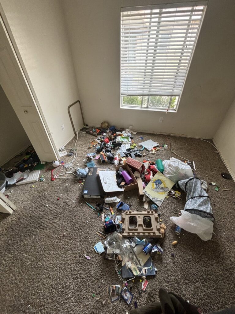A cluttered room with various debris scattered on the floor, indicating a cleanout job by YEE-HAul Trash Removal in St. George, UT.