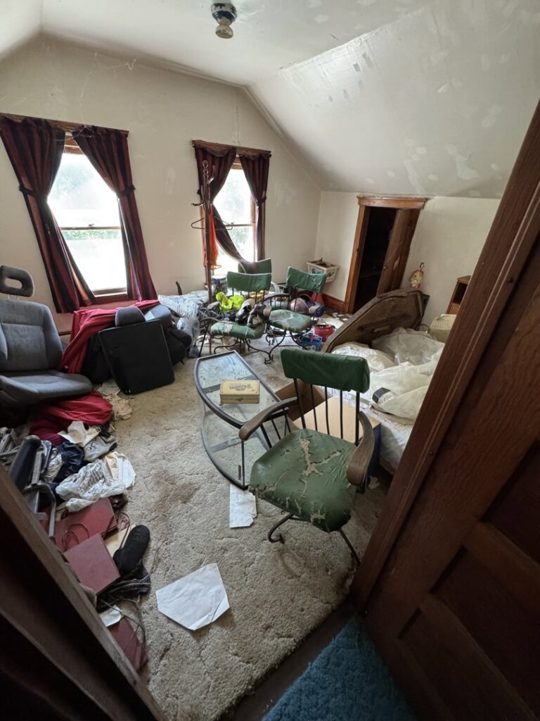 A heavily cluttered room with old furniture, clothes, and various items, indicating a major cleanout by Junk Removal Brothers in Worcester, MA.