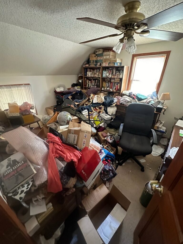 A heavily cluttered room filled with boxes, clothes, and various items, indicating a junk removal job for All Seasons Junk Removal & Dumpster Services in Center Point, IA.