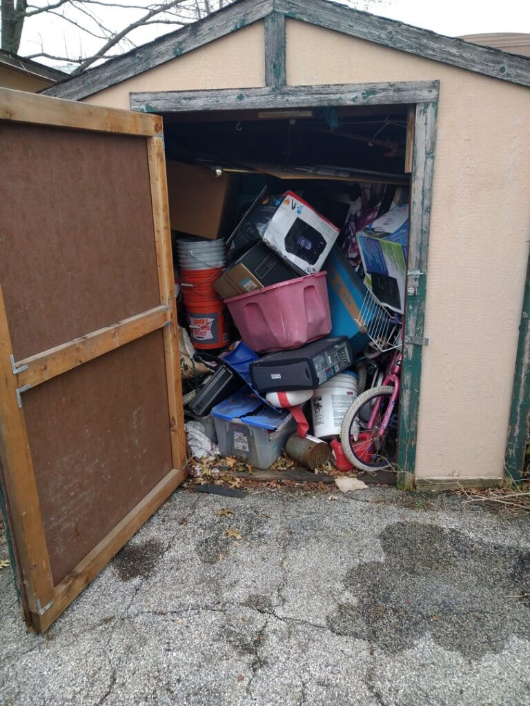 A shed completely filled with boxes, electronics, and various clutter, awaiting cleanout by Kaveman Hauling LLC in Ankeny, IA.