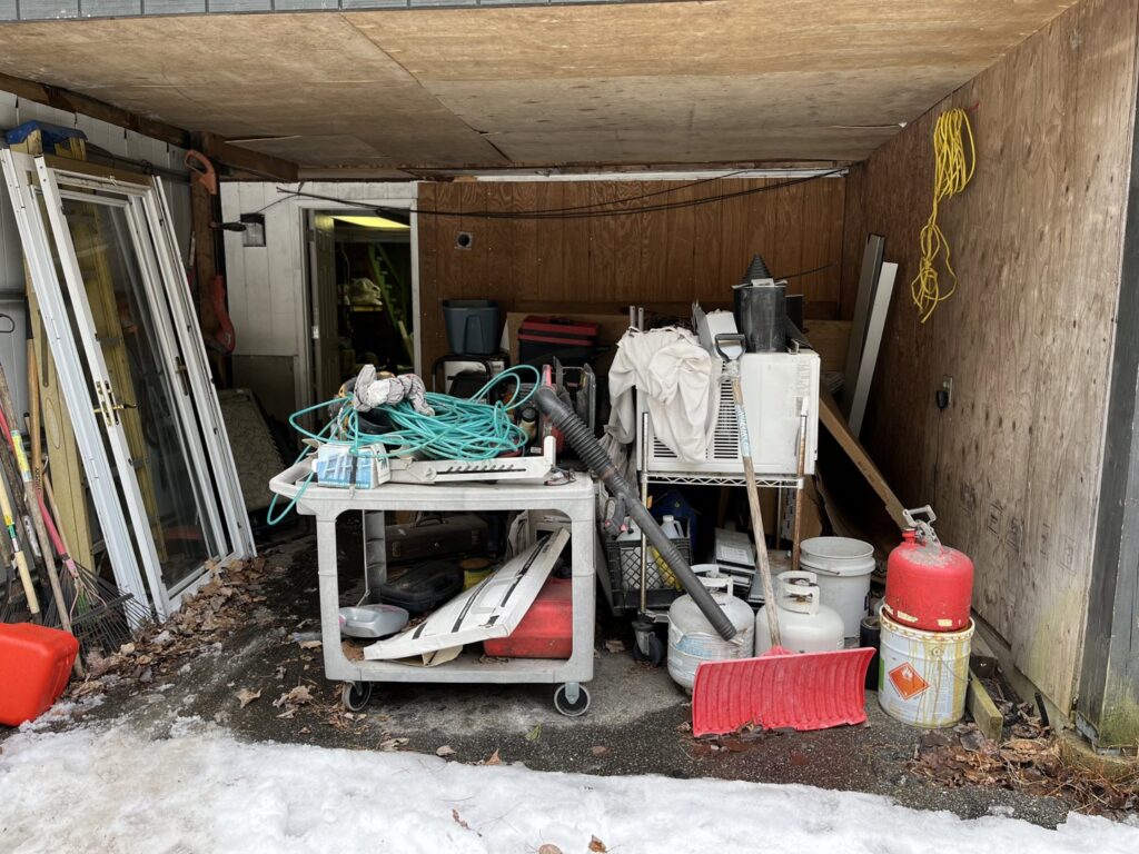 A cluttered shed or carport filled with various items before a cleanout service by Tj's junk removal LLC in Derry, NH.