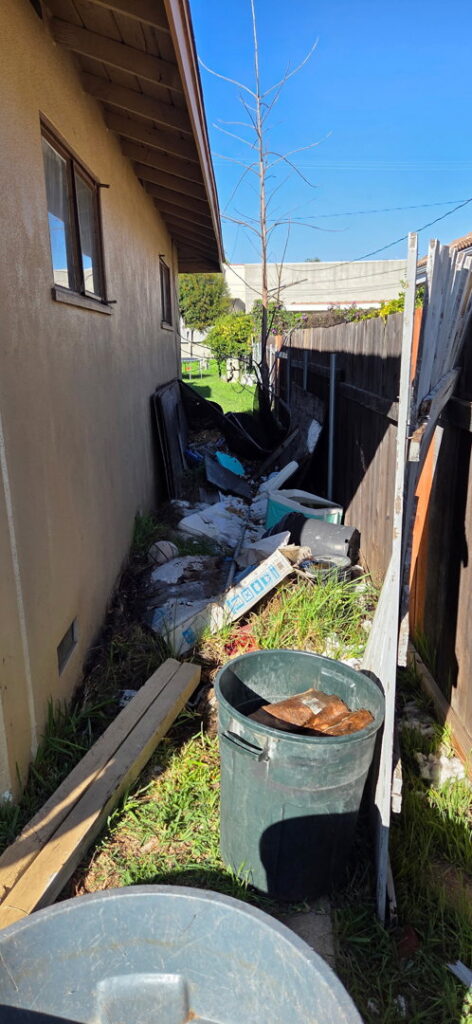 A cluttered side yard filled with various junk items, awaiting removal by New Haul Junk Removal in Los Angeles, CA.