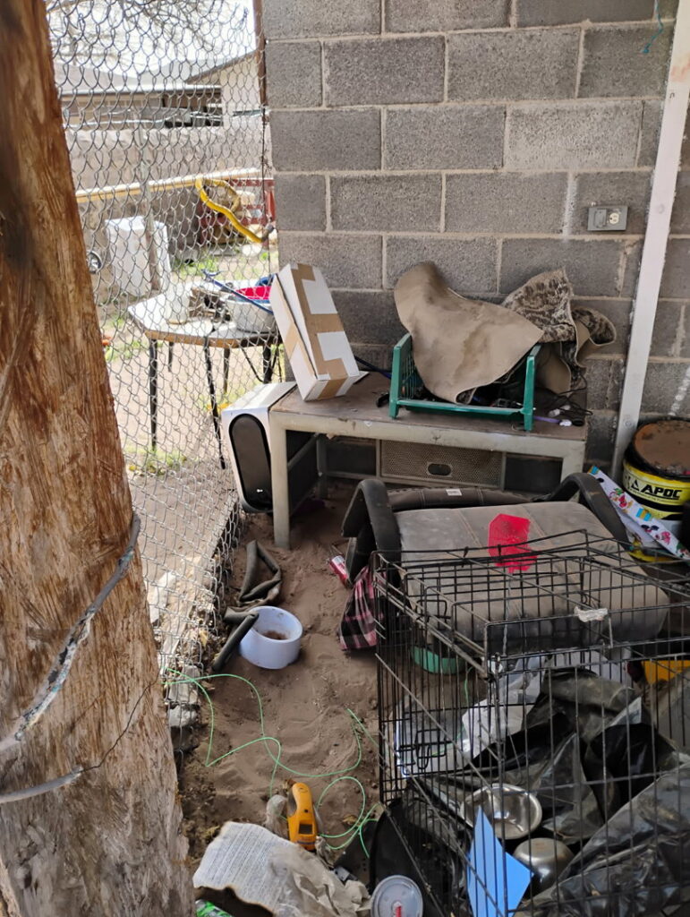 A cluttered outdoor area with various items and a dog crate, indicating a junk removal or yard cleanout job by Discount Hauling in Las Cruces, NM.
