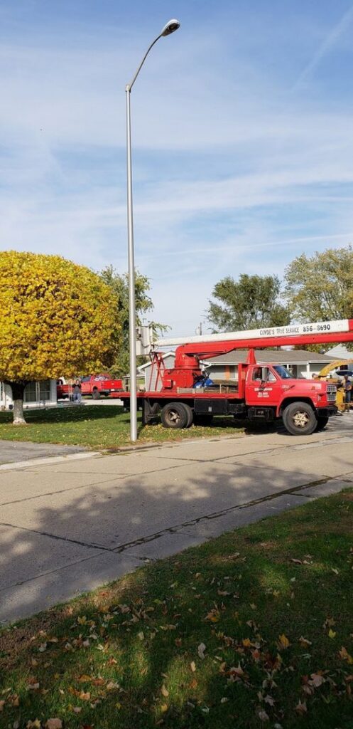 A red boom truck with 'Clyde's Tree Service' branding parked on a street in Indianapolis, IN, ready for tree work.