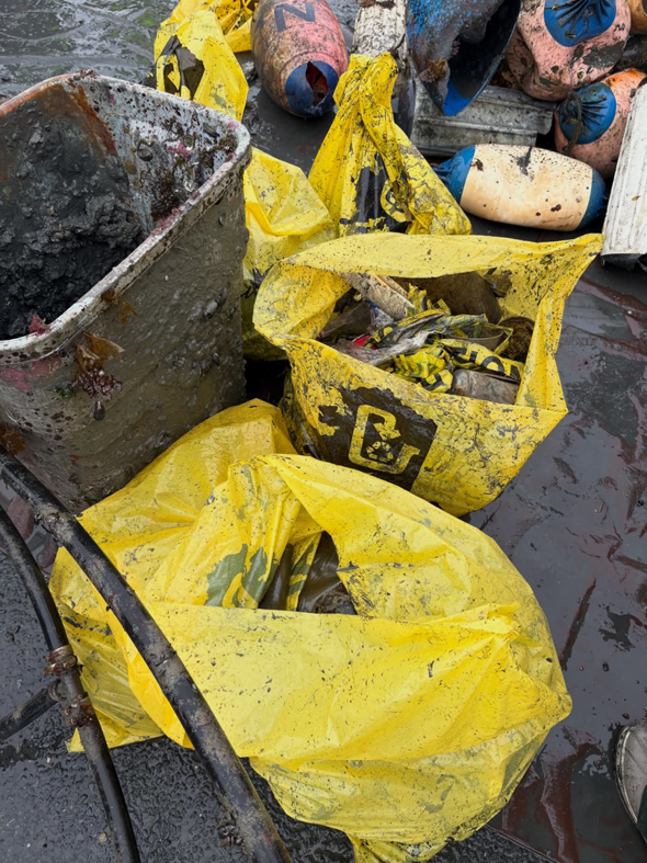 Collected junk and debris in yellow bags and a dirty bin, ready for removal by Alaska Waste in Anchorage, AK.