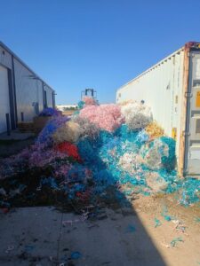 A large pile of colorful waste material next to a shipping container for T-Rex Service LLC in Cheyenne, WY.