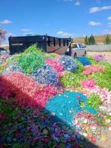 A large pile of colorful waste and plastic caps with a dump trailer for T-Rex Service LLC in Cheyenne, WY.