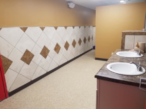 A renovated commercial bathroom with new wall tiling and double sinks by Land Bank Builders and Associates in Gary, IN