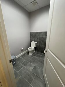 A newly remodeled commercial bathroom featuring dark tile flooring and an accent wall, completed by M7 Remodel & Restoration Inc. in Houston, TX