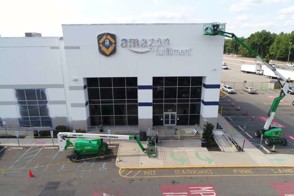 Workers on boom lifts performing exterior painting at an Amazon fulfillment center by Alpine Painting and Sandblasting Contractors in Paterson, NJ.