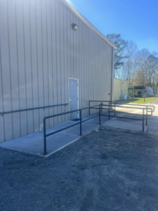 A newly installed concrete access ramp with black metal handrails for a commercial building by Boyce Welding, LLC in Courtland, VA.