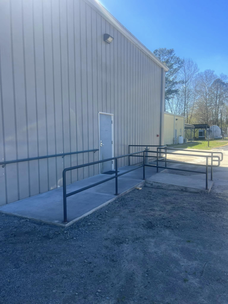 A newly installed concrete access ramp with black metal handrails for a commercial building by Boyce Welding, LLC in Courtland, VA.