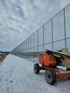 A long commercial chain-link fence installation with a boom lift on a snowy day by Fox Valley Fencing LLC in Appleton, WI