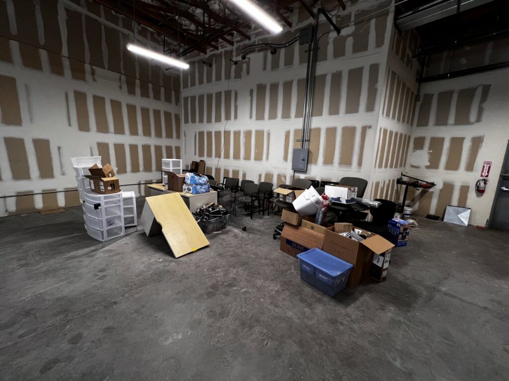 A commercial space, possibly a warehouse, filled with boxes, chairs, and various items, indicating a cleanout service by MLG Strong Hauling & Junk Removal LLC in Henderson, NV.