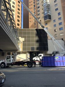 A crane loading commercial debris into a Toss-It dumpster in a bustling city environment in Glen Burnie, MD.