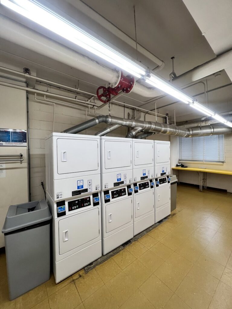 A row of commercial dryers in a laundry room, indicating a job site for Dryer Vent Cleaning of Delaware in Wilmington, DE.