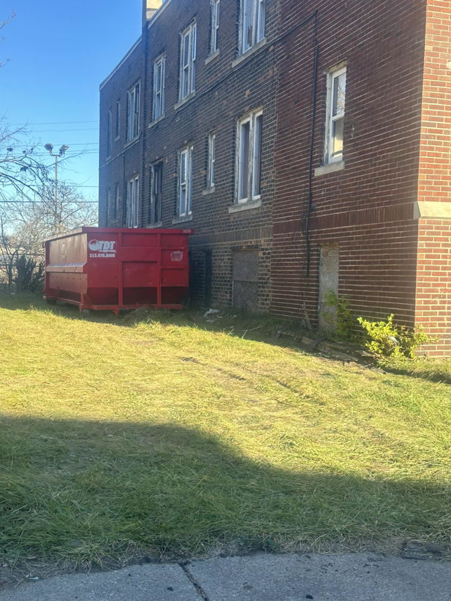 A red roll-off dumpster from The Dump Town placed next to a commercial brick building in Detroit, MI.