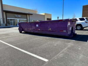 A purple dumpster from JP's Disposal Inc. placed in a commercial parking lot in Hampton, VA.
