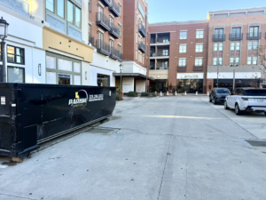A commercial dumpster from Parish Dumpsters, LLC placed in an urban area near buildings in Baton Rouge, LA.
