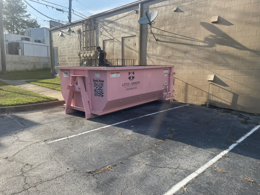 A pink dumpster from Little Junkers placed in a commercial parking lot for business junk removal in Peachtree City, GA.