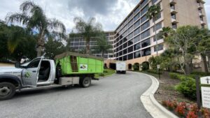A truck with a green dumpster providing commercial junk removal service for Bin There Dump That Dumpster Rental Orlando, FL.