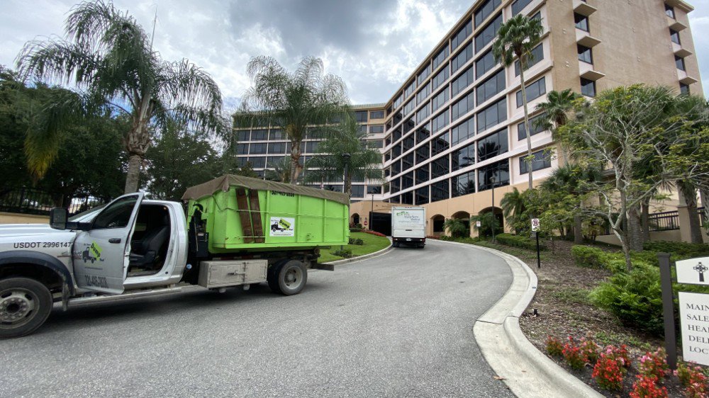 A truck with a green dumpster providing commercial junk removal service for Bin There Dump That Dumpster Rental Orlando, FL.
