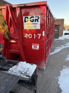 A Geppert Recycling truck providing commercial dumpster service, partially covered in snow, in Philadelphia, PA.