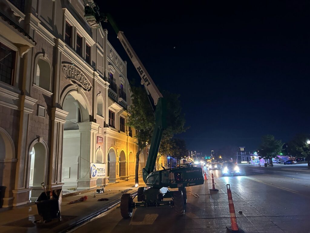 Commercial exterior renovation work at night with a boom lift and Ricos Renovations signage in Arlington, TX