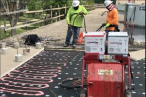 Workers applying a new membrane to a commercial flat roof using specialized equipment for Total Improvements LLC in San Antonio, TX