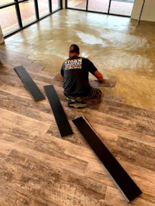 A skilled worker installing wood-look vinyl plank flooring in a commercial space for Stormtroopers Home Improvement in Port St. Lucie, FL.