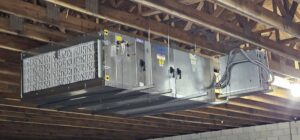 Large commercial HVAC unit suspended from a wooden ceiling during installation by Belair Inc. in Saint Cloud, FL